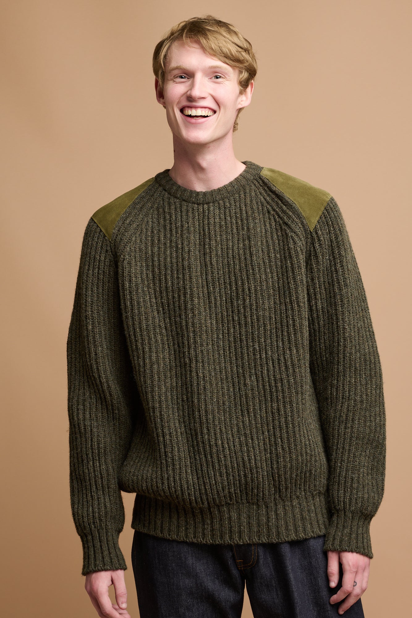 Thigh up image of smiley male with blonde hair wearing lambswool fisherman ribbed jumper in dark live 