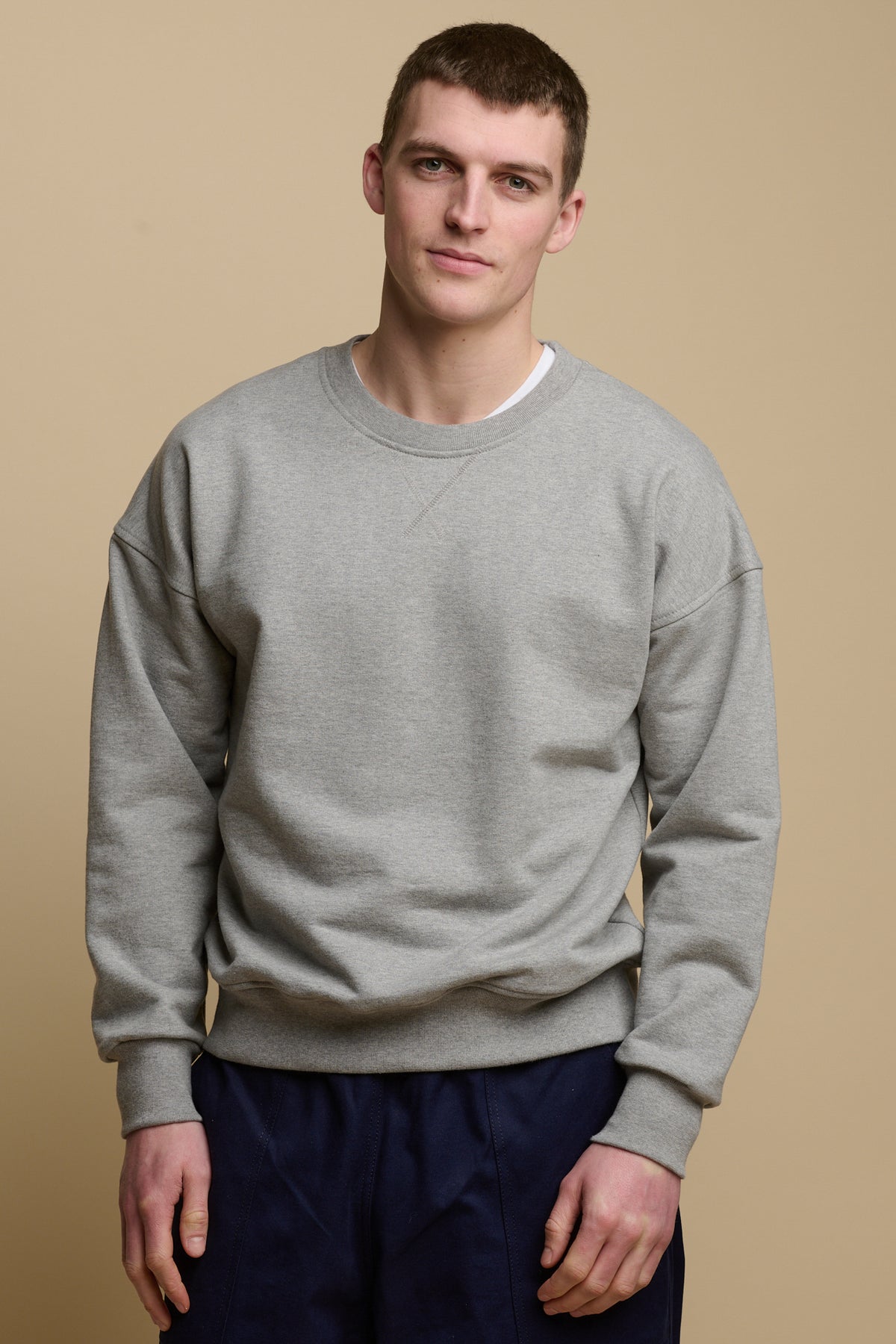 
            Thigh up front of brunet male wearing men&#39;s heritage drop shoulder sweatshirt in grey, worn over crew neck white t shirt paired with cameraman pants in navy
